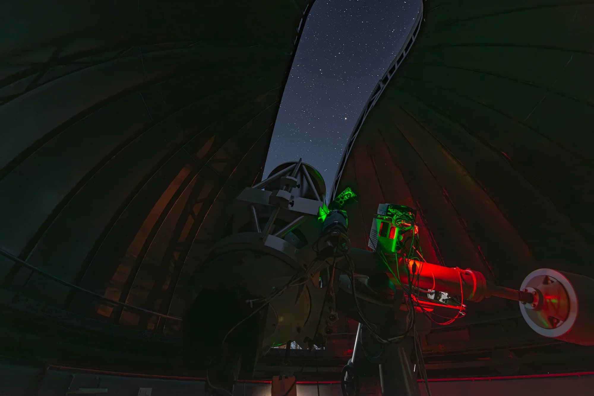 Interior of an observatory with a slightly opened dome and BLT telescope aimed at the night sky.