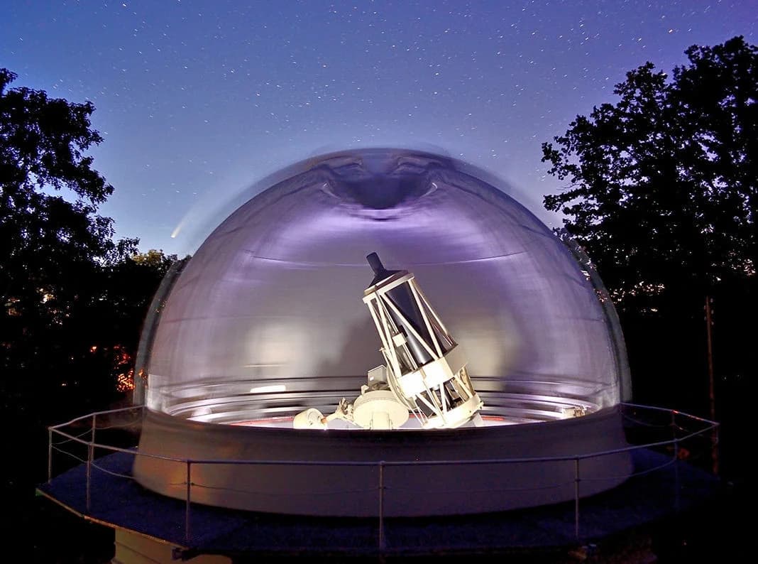 Observatory dome at night with a BLT telescope illuminated inside, under a starry sky.